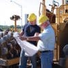 Two construction workers hold architectural plans while reviewing them.