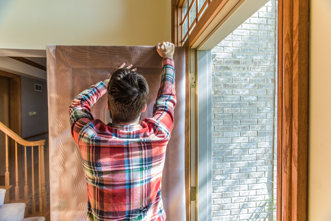 A man installing a protective plastic surface for doors.