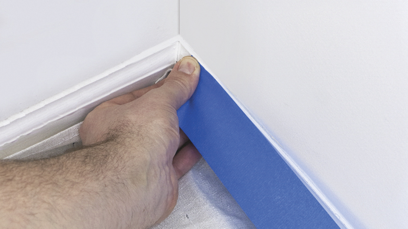 blue painter's tape being applied to white baseboard