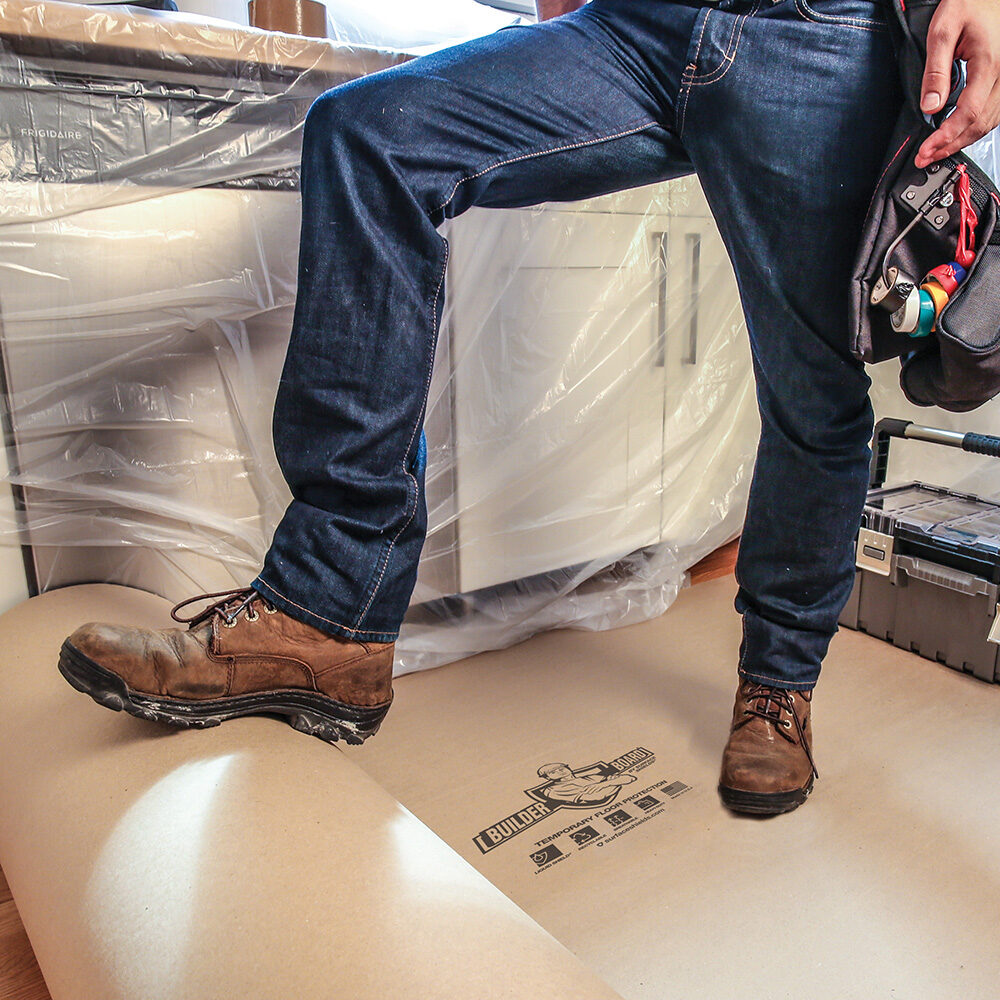 man in boots kicking out a roll of floor protection board in a kitchen prepped for construction