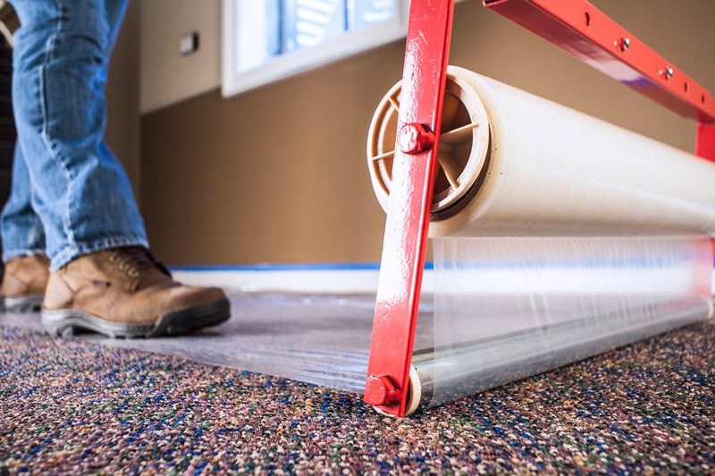 A man using a large self-adhesive protective film on a carpet.