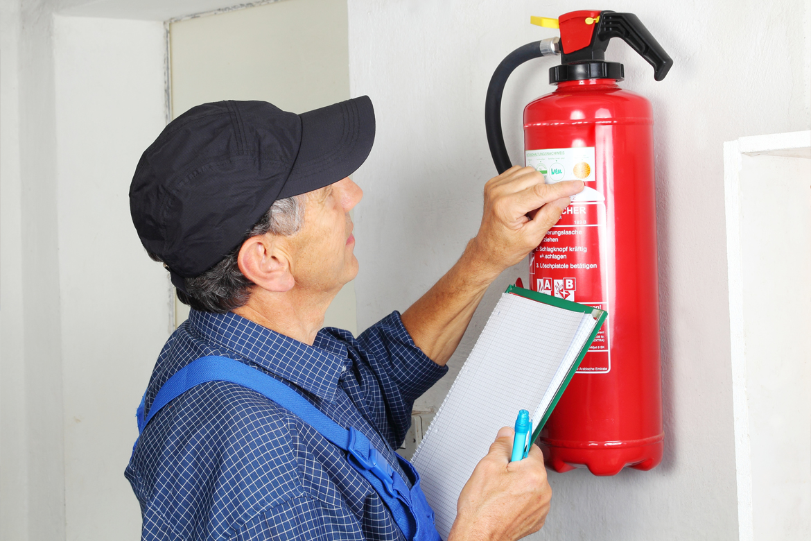 A man checking the expiration date of a fire extinguisher attached to the wall.