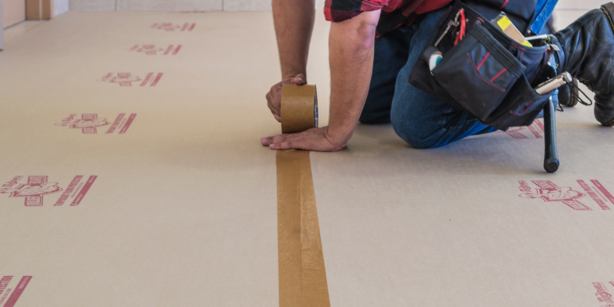 A man crouching over several protective surfaces while taping them together.