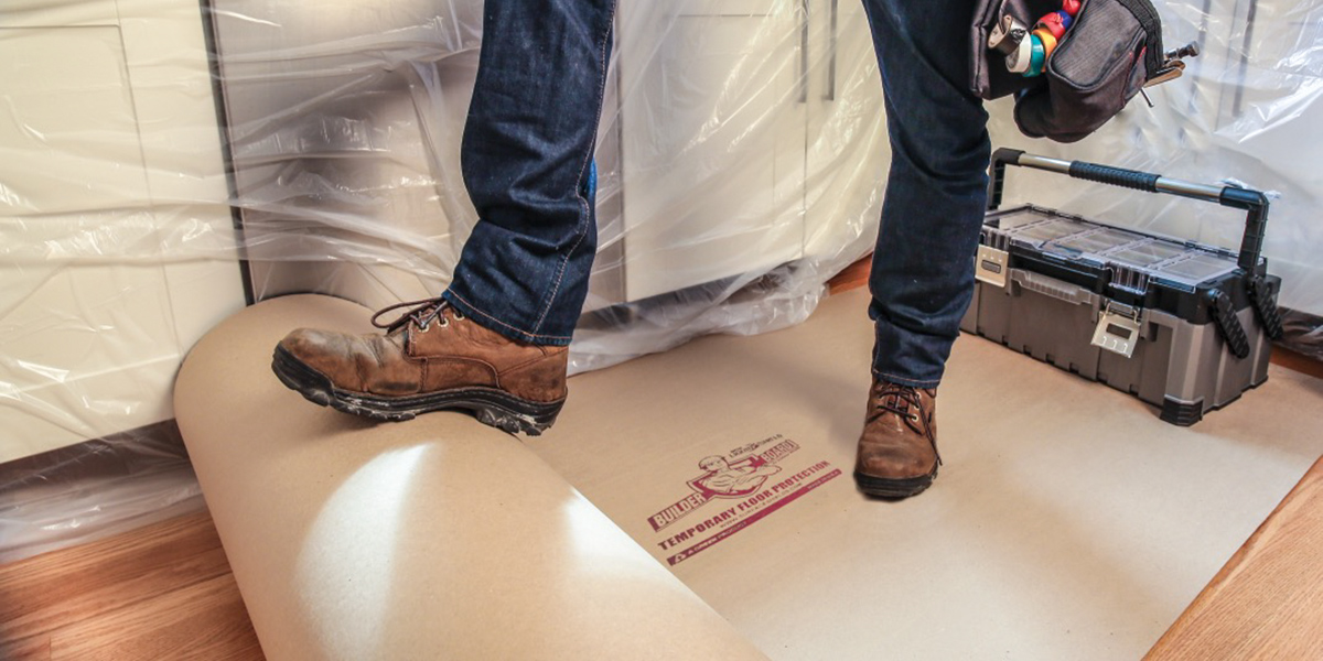 A man holding a roll of protective cardboard with his foot.