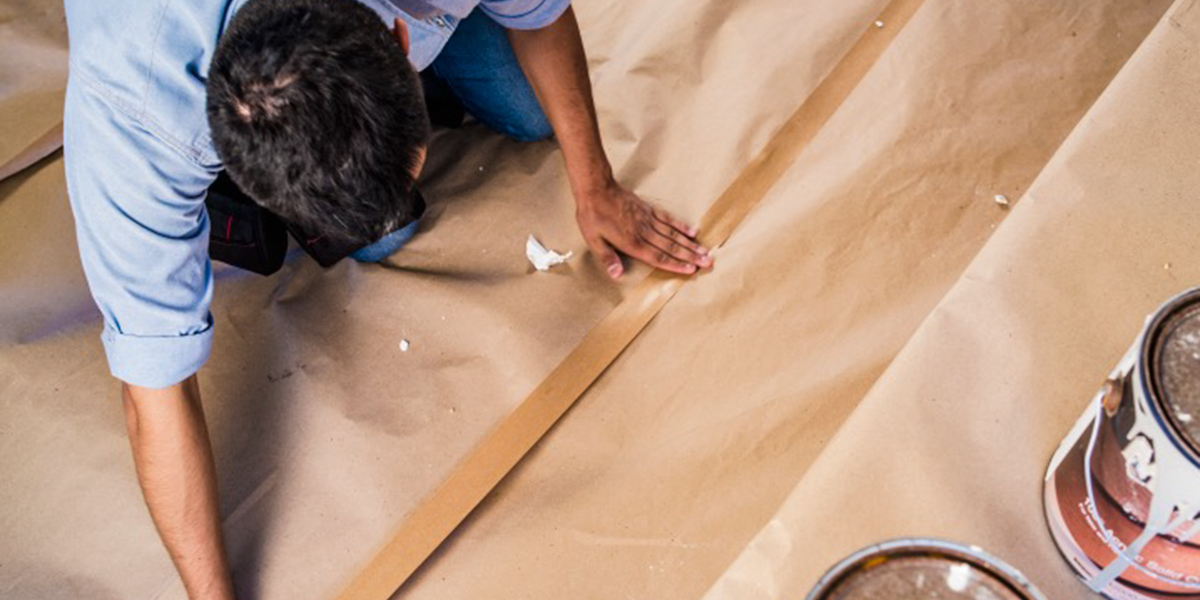 A photo from above of a man who is joining two segments of protective paper with adhesive tape.