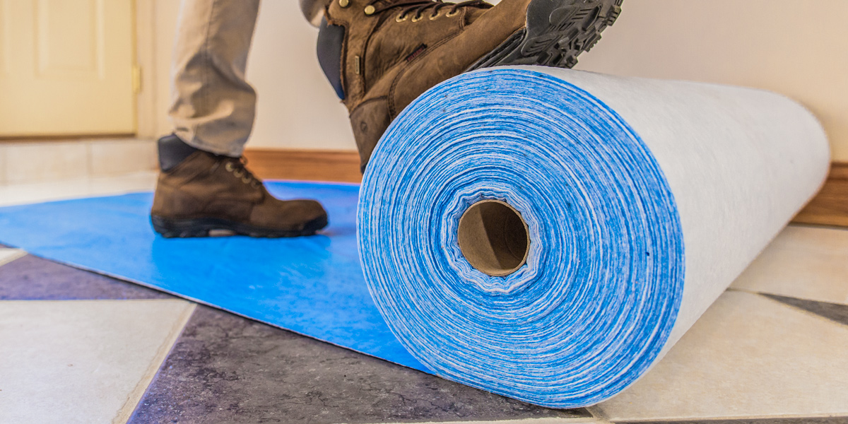 A man unrolling a blue protective material with his feet.