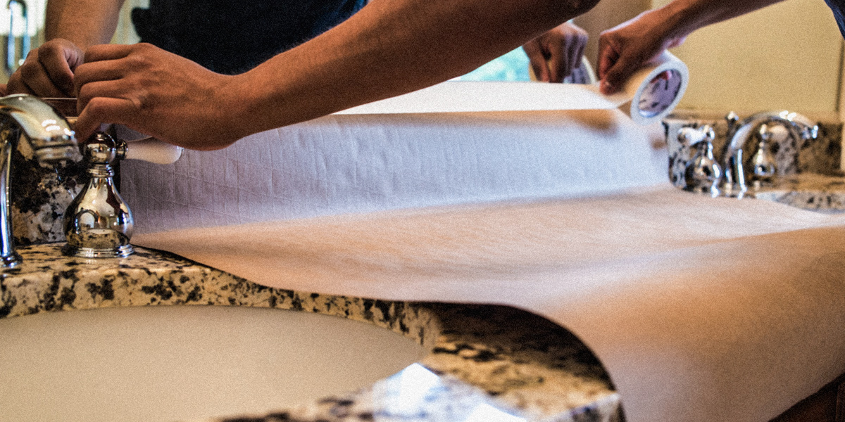 Photo of a man's hands as he puts protective paper on the surface of a bathroom sink.