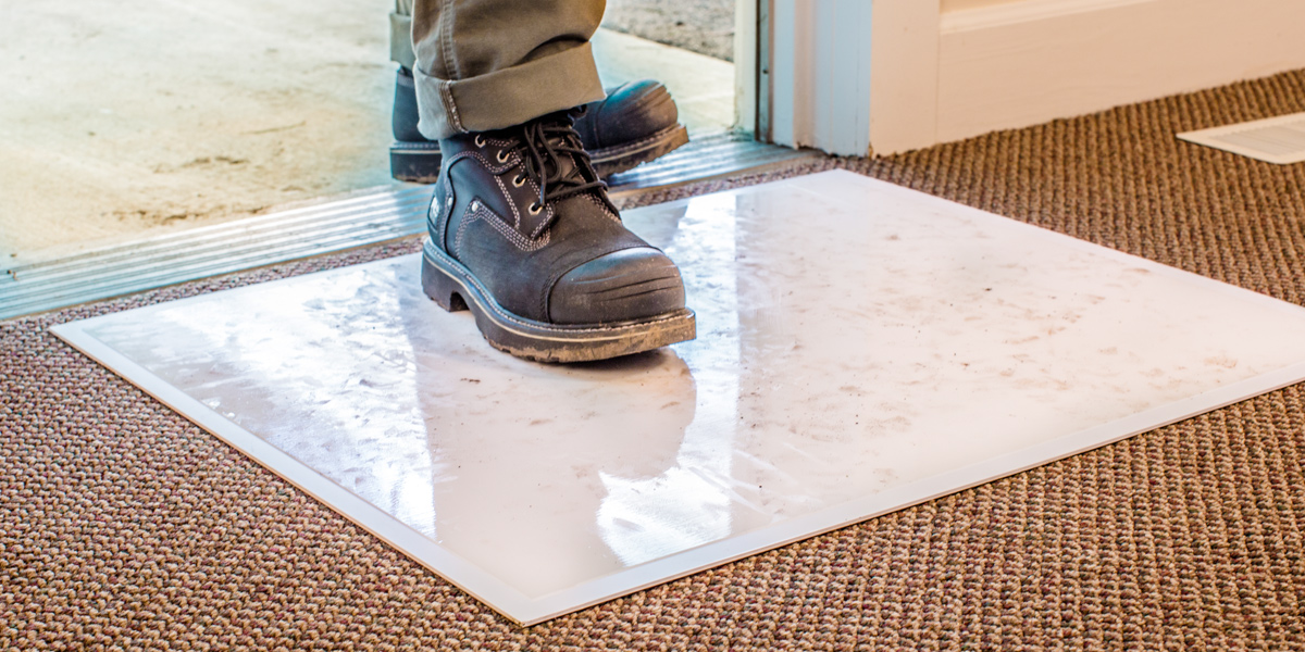 A close-up of a man's dirty shoes while standing on a protective surface on a carpet.