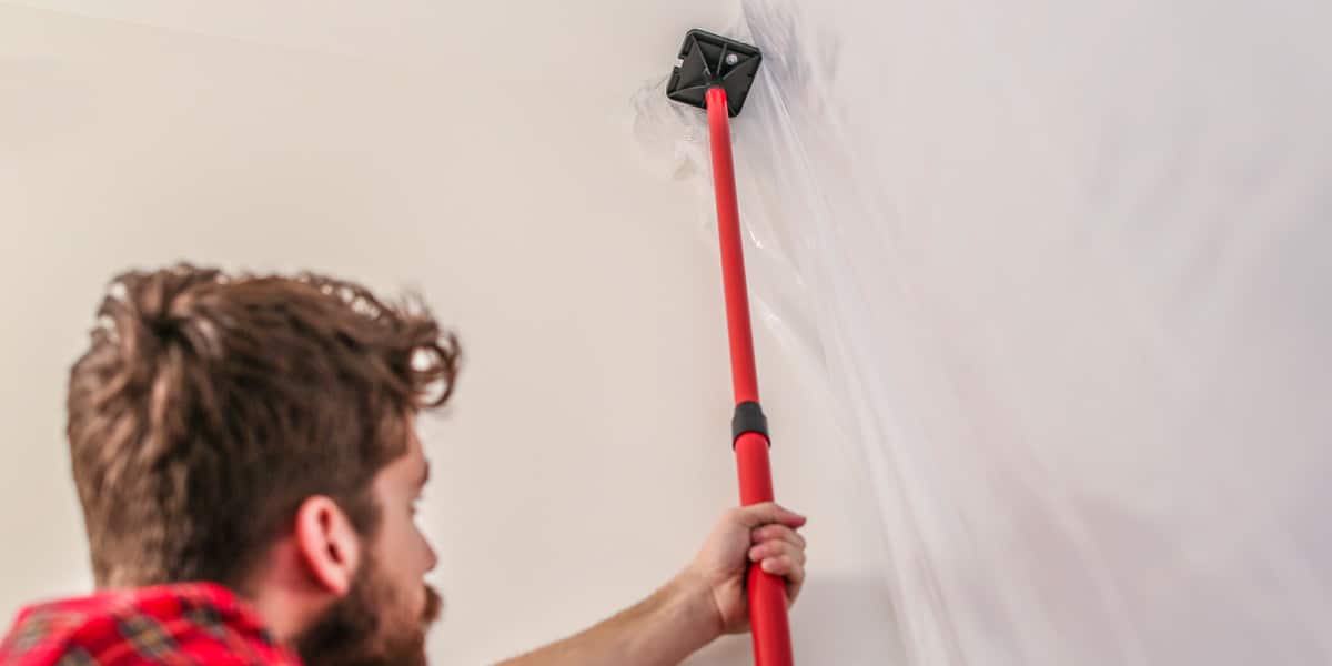 A man holds a plastic against the ceiling with a red and black pole.