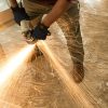 A man uses a metal polishing machine as filings fall onto a carpet protected by protective tape.