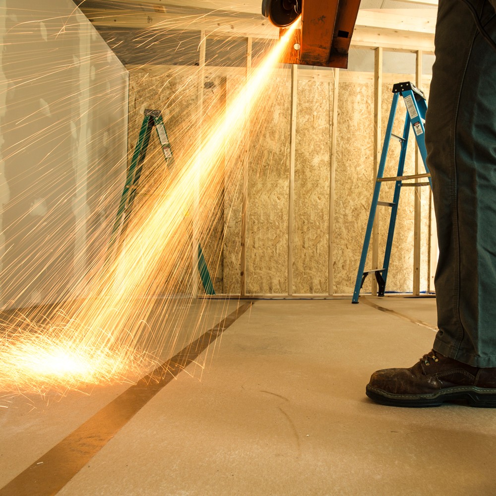 A man uses a metal polishing machine as filings fall onto a carpet protected by protective tape.