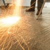 A man uses a metal polishing machine as filings fall onto a carpet protected by protective tape.