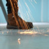 A man uses a metal polishing machine as filings fall onto a protective surface.