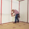 A man uses a red tape to attach surface protectors to the walls of a room.