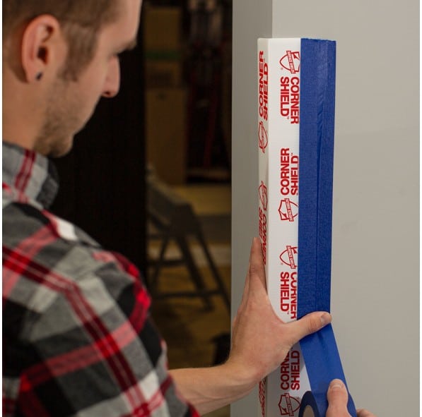 A man installing a corner protection surface with blue tape.