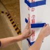 Photo of hands putting blue adhesive tape on a corner protective surface.