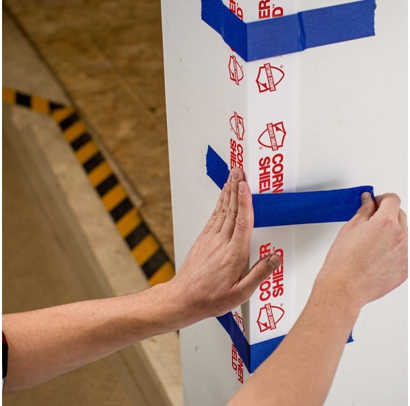 Photo of hands putting blue adhesive tape on a corner protective surface.