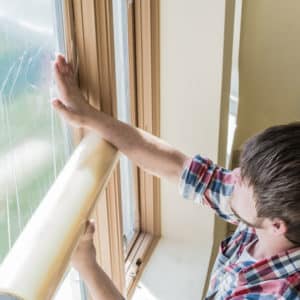 Man smoothing a window protection film over a window inside a house