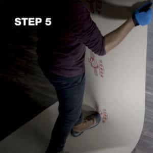 man with gloves pulling floor protection board, builder board, up as he steps in the center