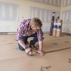 man applies builder board seam tape to floor protection on a construction site.