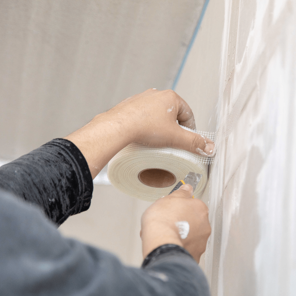man applying white drywall scrim tape to sheetrock